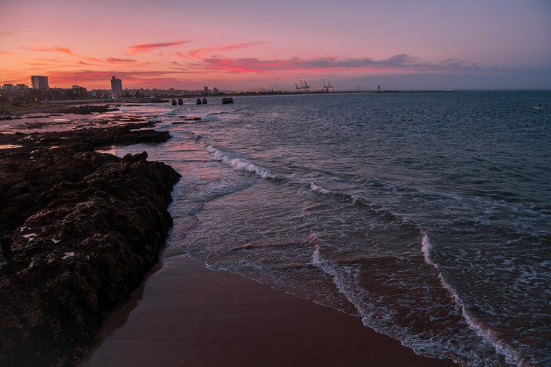 ocean washing on the shoreline near the city at sunset, shoreline at sunset 4k