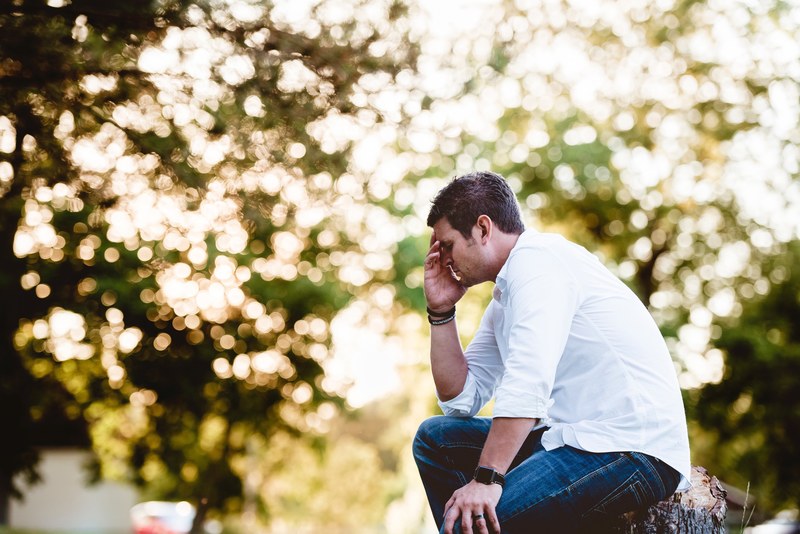 a man wearing a white button up shirt and jeans sitting on a tree stump thinking, sad man thinking 4k
