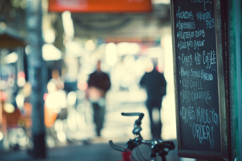 a menu is written on a chalkboard hanging outside of a cafe on the street, cafe menu 4k