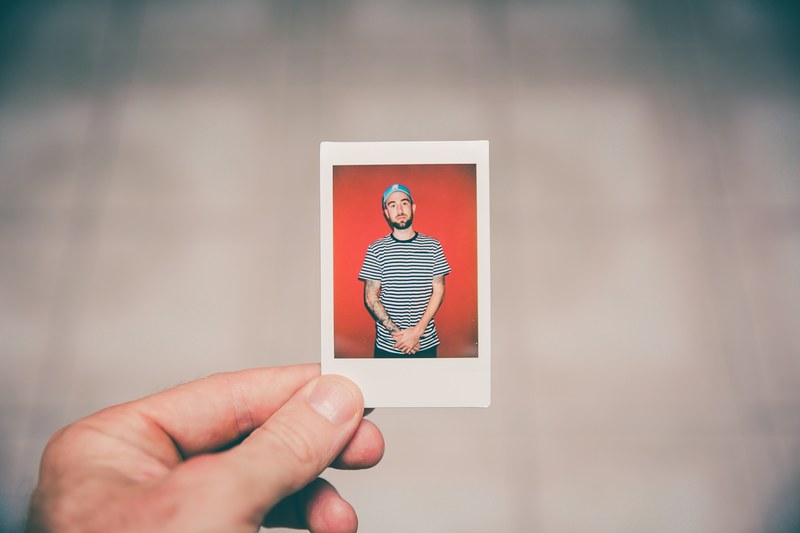 hand holding a photograph of a man in a striped shirt with tattoos wearing a baseball cap, hand holding photo 4k