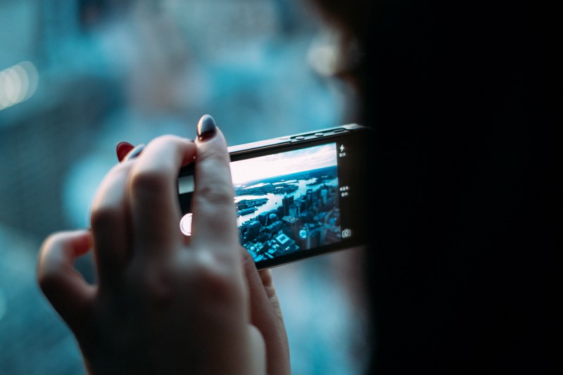 macro of a woman with dark red nails taking a photo of the city on her iphone, iphone photos 4k