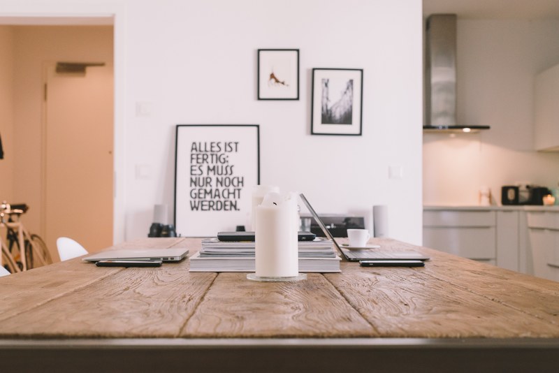 apartment interior with wooden table and framed artwork on white wall with white candle on table, wood table in front of white wall 4k