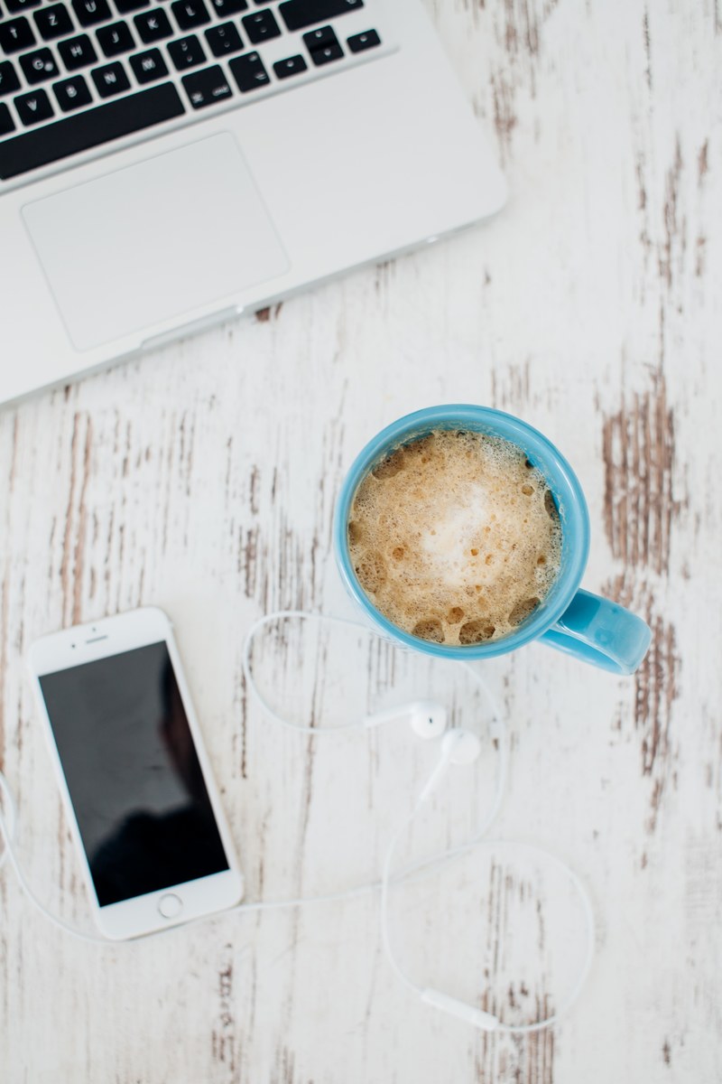 an overhead shot of a cup of coffee next to an iphone and a macbook, overhead view of coffee mug on office table 4k