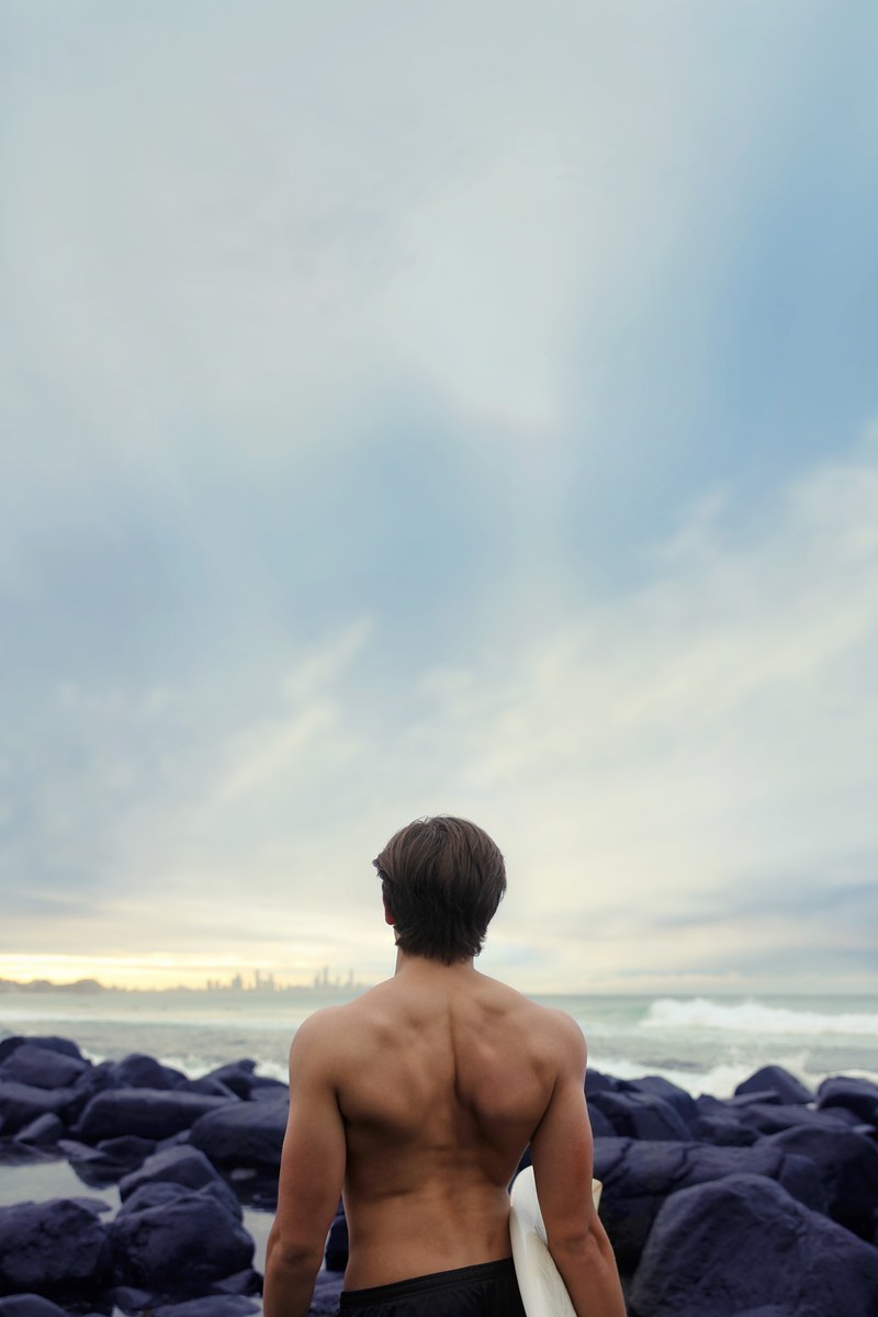 topless man standing among coastal rocks looking in the distance at burleigh beach, topless man standing on beach 4k