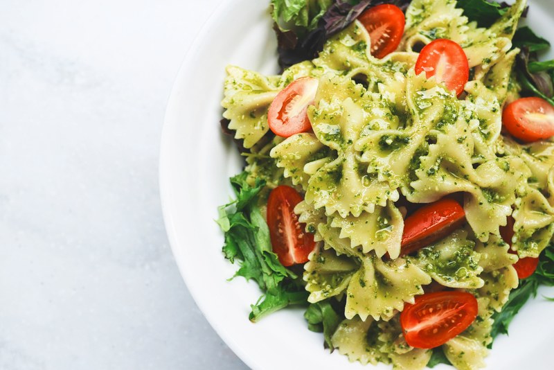 a plate of bow tie pasta cherry tomatoes lettuce and pesto sauce at bunas kitchen, pesto pasta 4k