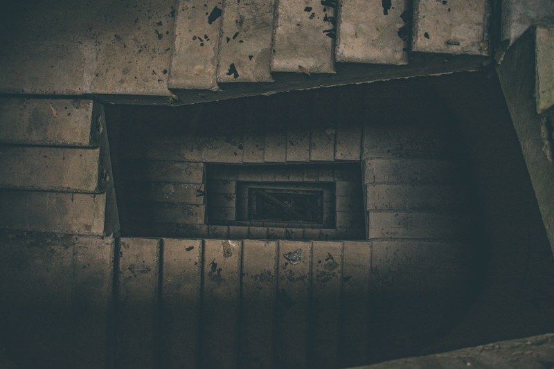 looking down at a dark disused brown coloured rectangular stairwell, urbex 4k