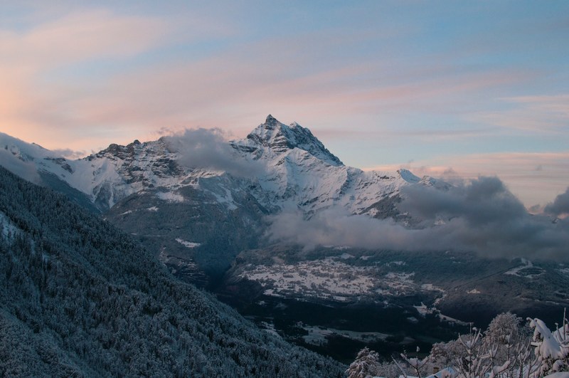 tall snow covered mountains towering over a wooded valley, forest valley in the snowy mountains 4k