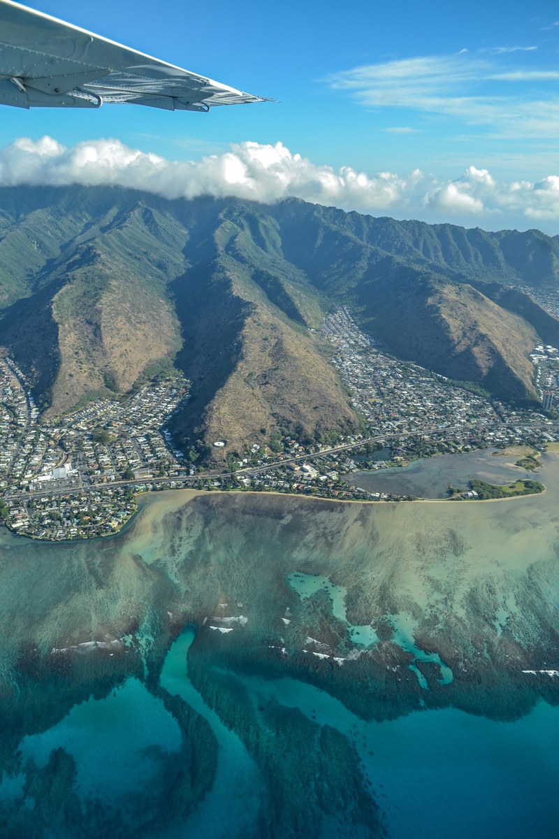 aerial view of a mountain town along the coast from a plane in oahu, wondering what their lives are like 4k