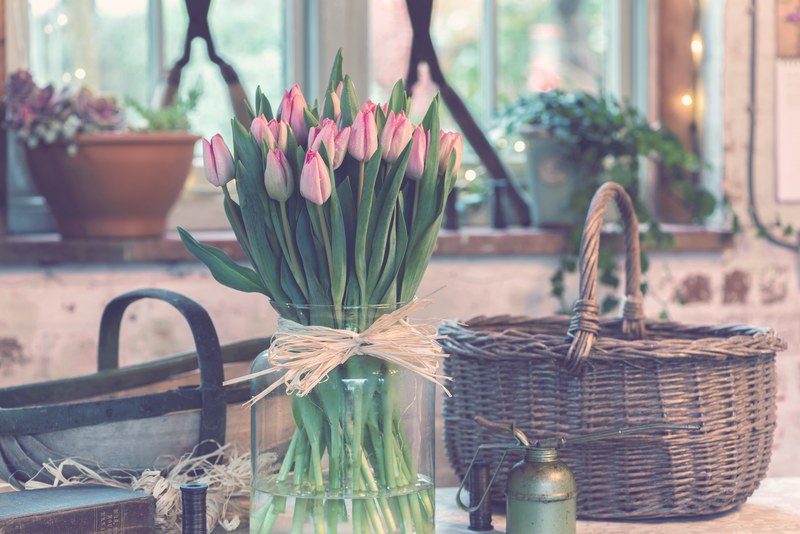 a large glass vase filled with pink tulips next to a wicker basket, rustic tulip vase 4k