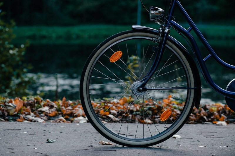 front half of a navy blue bicycle with wheel and spokes on a sidewalk near leaves, navy bicycle with wheel 4k
