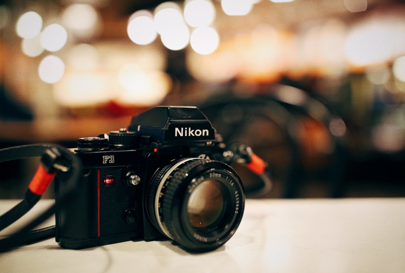nikon f3 camera on a white surface beside orange background, nikon f3 camera 4k