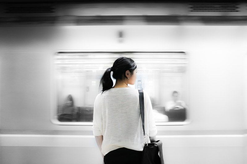 a subway train passing in front of a woman with a black leather bag, woman at a subway station 4k