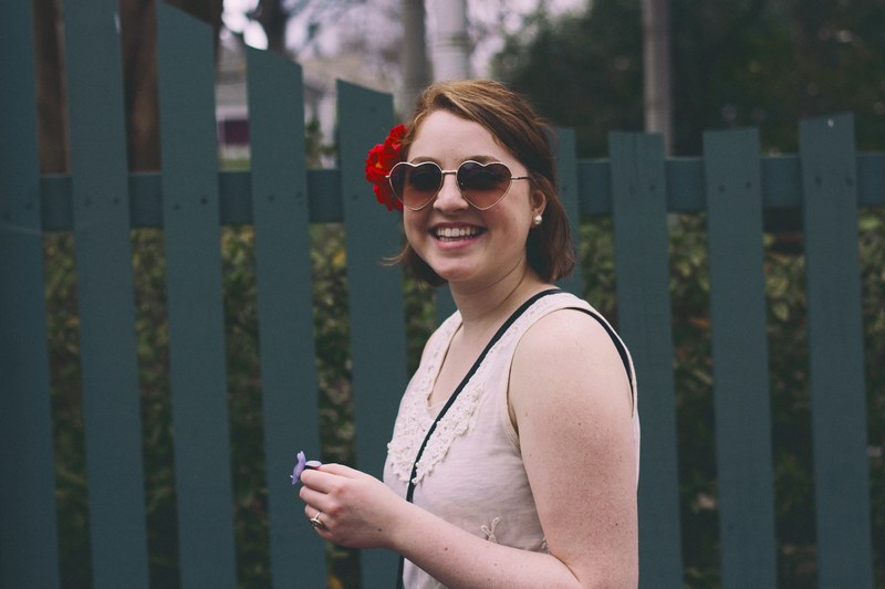 a smiling woman in heart shaped sunglasses with red flowers in her hands, joyful woman in heart sunglasses 4k