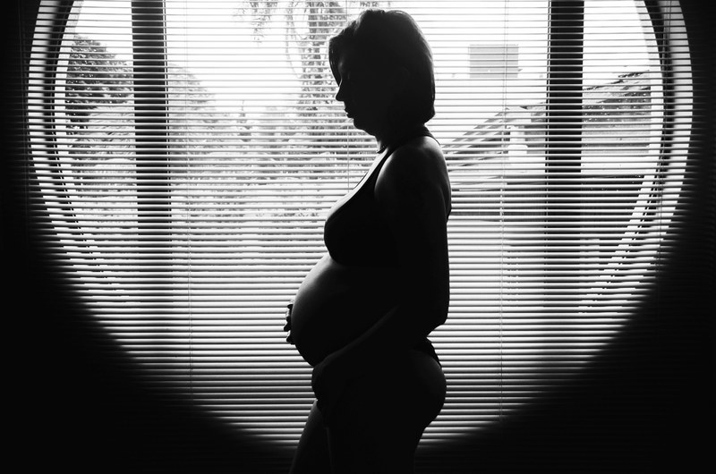 the black and white silhouette of a pregnant woman standing in front of a round window, _silhouetted baby bump 4k