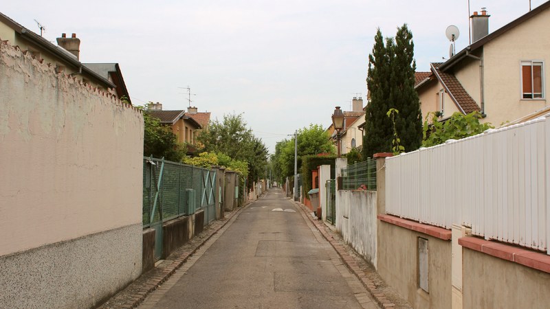 street in an urban setting with fences surrounding houses along the road, streetview 4k