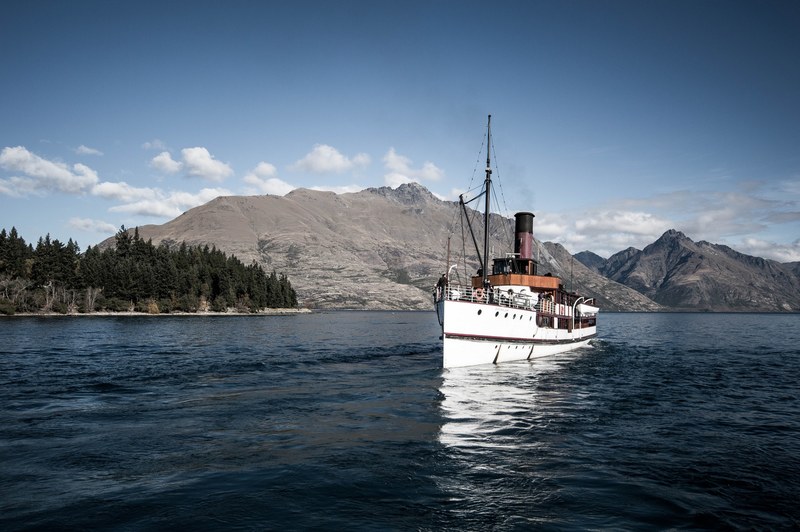 a boat sailing on the choppy surface of a lake with rocky hills on the shore, queenstown lake boat 4k