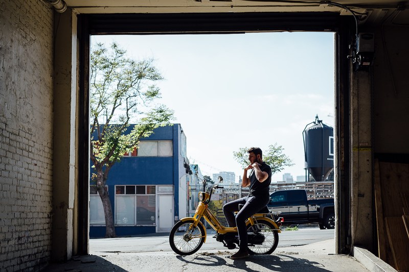 a man on a yellow moped in front of a white brick garage at moniker warehouse, moniker warehouse moped 4k