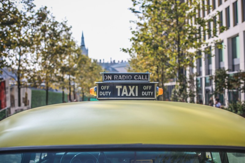 close up shot of top of yellow london taxi cab sign on road with trees, taxi cab in london leafy street 4k