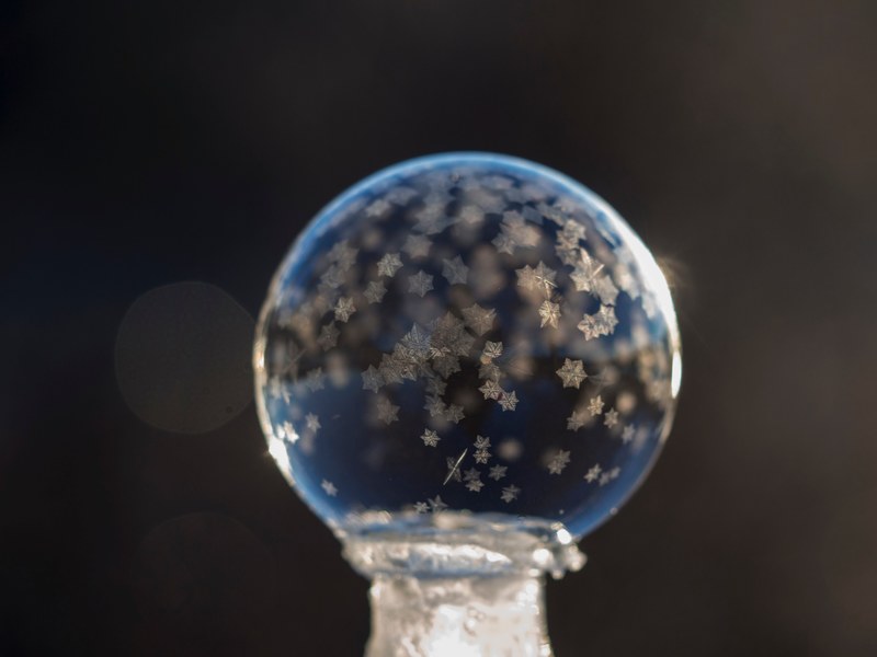 macro of a frozen bubble with small snowflakes with a black background, tiny frozen bubble snowflakes 4k