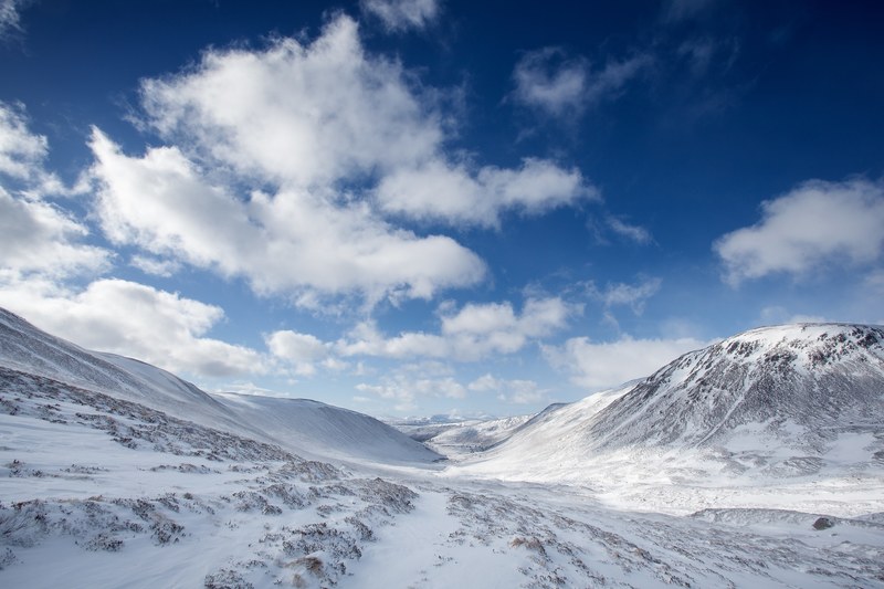 a snow filled valley in between mountains and a cloudy blue sky in cairngorms national park in scotland, snow mountain cloud and hill 4k