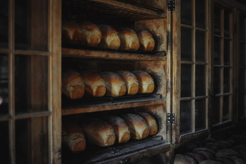 loaves of baked bread in an old looking bakery on three wooden shelves with glass windows, loaves of bread 4k