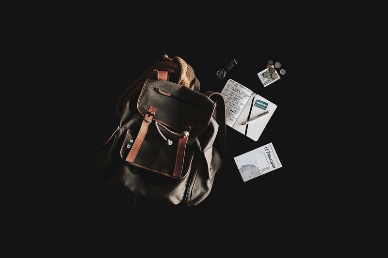 a backpack a watch a little prince book and coins against a black background, traveling flatlay 4k