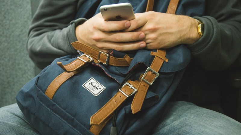 a man with a blue backpack on his lap using an iphone, texting while traveling 4k