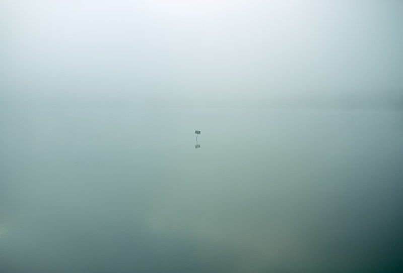 single isolated sign sits in eerie still waters covered in clouds, eerie isolation 4k