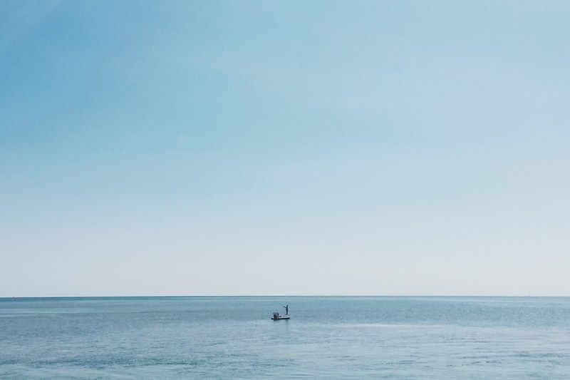 a fisherman on his boat on the calm ocean where the water meets the horizon, distant fisherman in the sea 4k