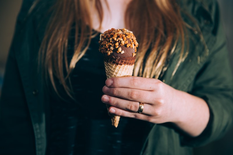 a woman holding a chocolate ice cream cone sprinkled with nuts, indulgent sweet treat 4k