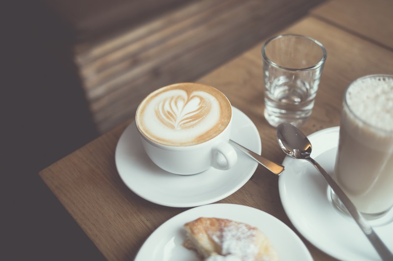 a cup of coffee with latte art next to a tall latte and a sweet pastry, coffee and a sweet treat 4k