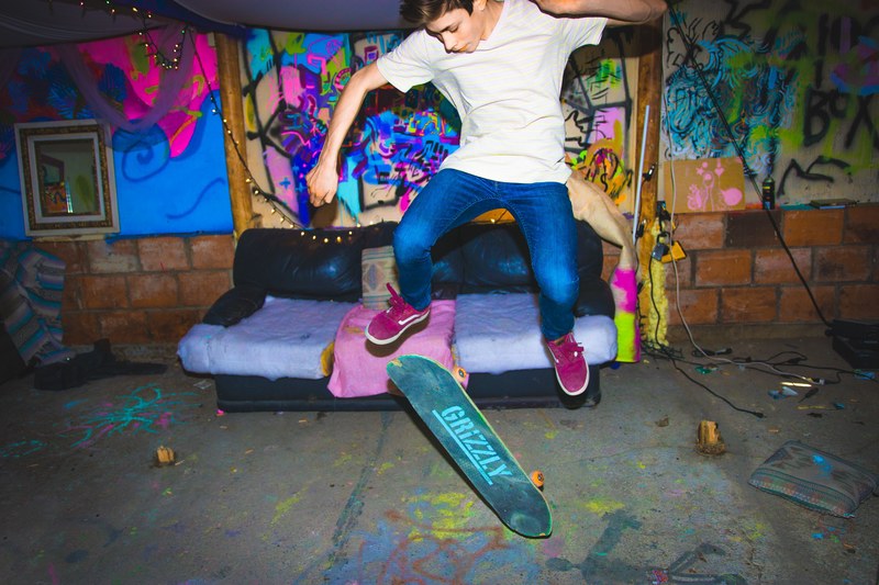 a skateboarder does a trick in front of a couch and neon graffitied wall, skateboarder in front of couch 4k