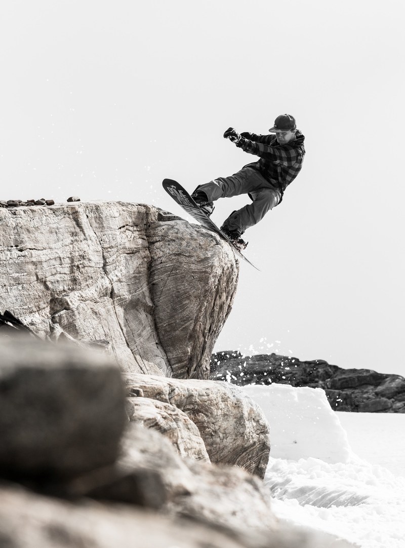 a snowboarder performs a trick and stalls on a boulder on a snowy mountain, sliding rocks 4k