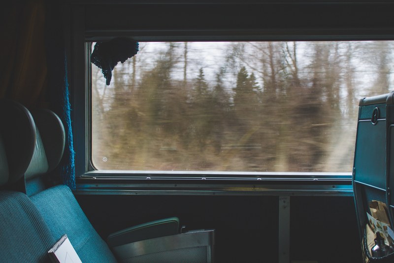 the interior of a moving train with empty seats next to a window, flickering trees outside a train window 4k