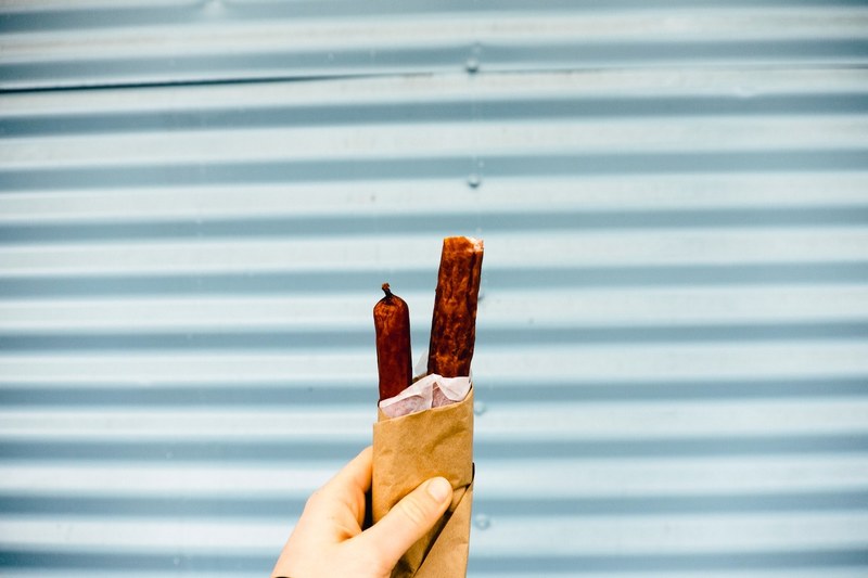 outstretched hand holding sausage snacks against a gray garage, sausage snacks 4k