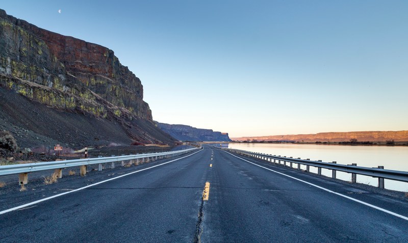 an asphalt highway surrounded by mountains on one side and water on the other, highway views 4k