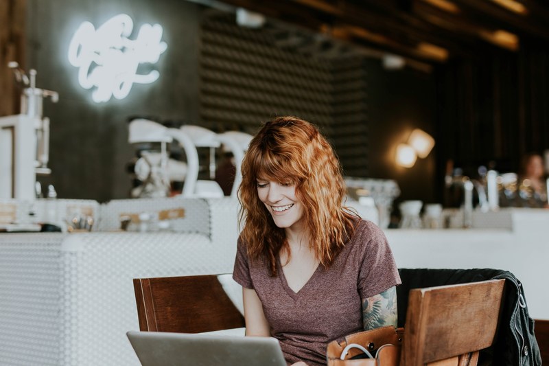 a young woman smiling while looking at a laptop screen at a coffee shop, tattooed woman with laptop 4k