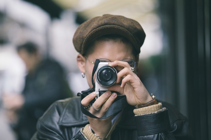 a person wearing a hat taking a photo with a white sony camera on brewer street, brewer street photographer 4k