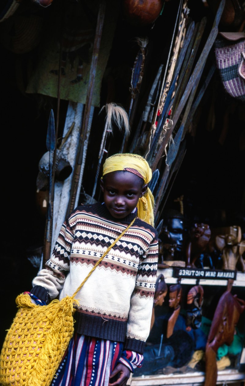 child in a colorful outfit with a yellow bag at an outdoor market, child by market stall 4k