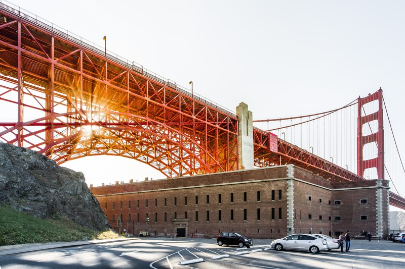 san francisco golden gate bridge at sunset suspended over a brown building cars and people, golden gate bridge sunset 4k