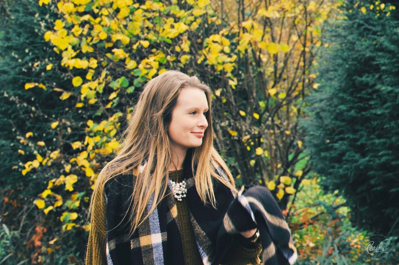 a long haired woman wearing a blanket smiles to the side in front of trees, smiling woman in blanket 4k
