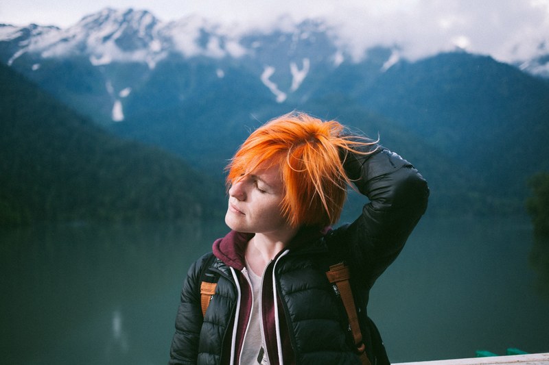 a woman closes her eyes and places a hand in her orange hair in the mountains, orange hair woman in mountains 4k