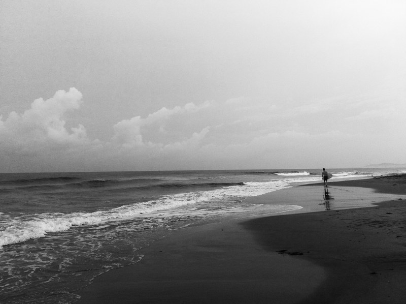 a black and white shot of a person walking a deserted beach beneath a cloudy sky, black and white beach 4k