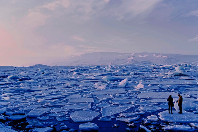 people looking at frozen ice sheets breaking apart in the water with a mountain view, watching breaking ice sheets 4k