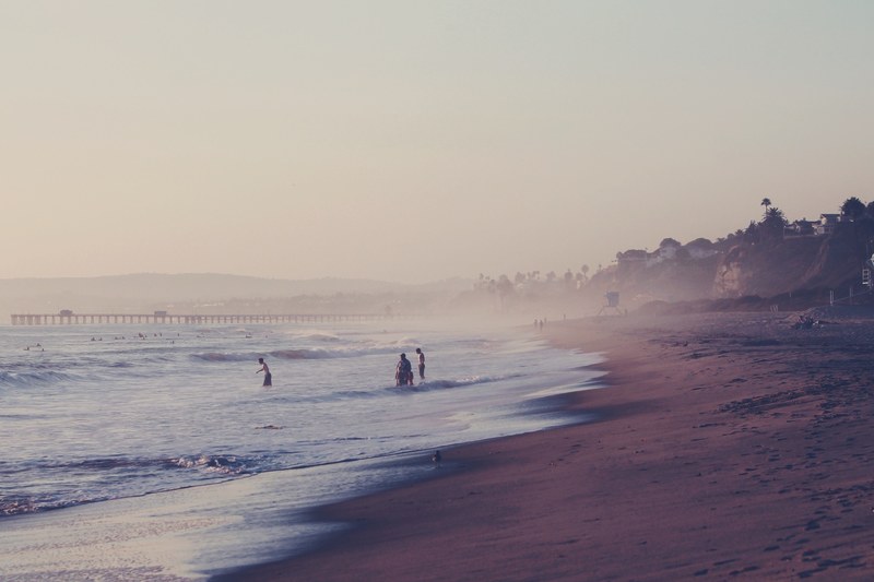 people swimming at the beach by the sea shore with tide and a bridge in the background, _swimming at the beach 4k