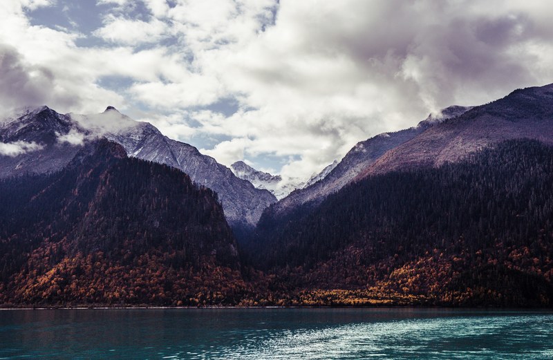 view from an azure lake on tall wooded mountains at the shore, mountain lake in the autumn 4k