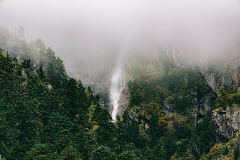 a waterfall pouring down a tall rock face with its top shrouded in mist, waterfall on a misty rock face 4k