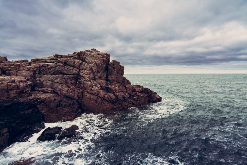 foaming waves around a rock formation beneath a cloudy sky at le gouffre, waves around the rocks 4k