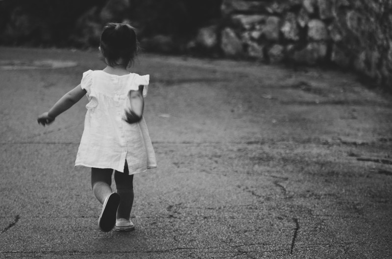 black and white shot of lone young child running in white dress on pavement in montpellier, little girl on the road 4k