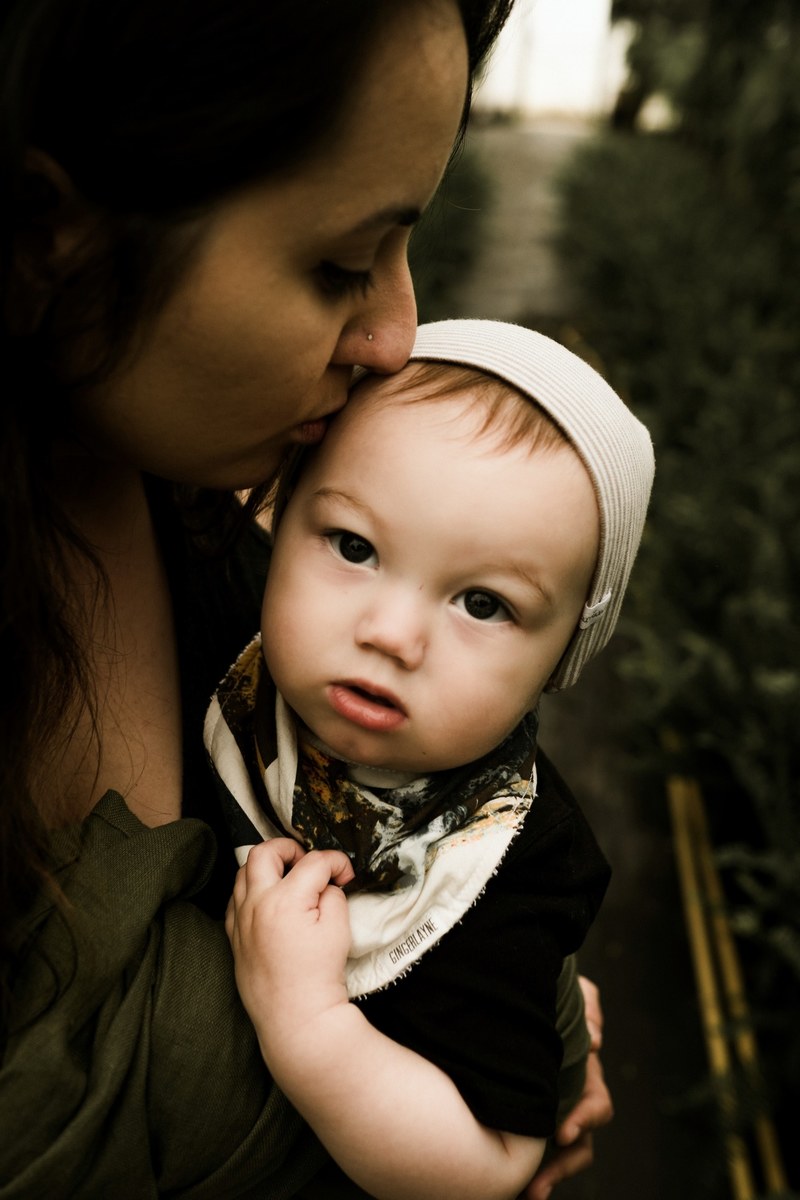 a brunette mother affectionately kissing the forehead of her young toddler who is wearing a white hat, a kiss from mom 4k